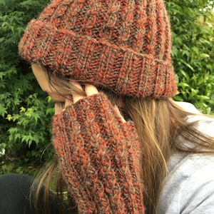 May include: A brown and orange knitted beanie and matching fingerless gloves. The beanie has a ribbed texture and the gloves are long and cozy.