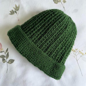 Könnte beinhalten: Eine dunkelgrüne Strickmütze mit gerippter Struktur. Die Mütze ist am Rand umgeklappt.