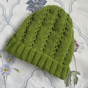 May include: A green knitted hat with a diamond pattern and openwork design.