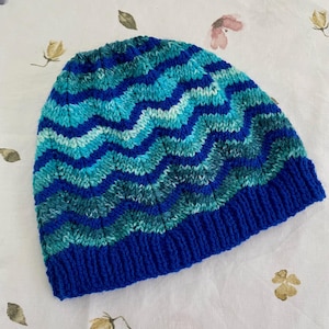 May include: A blue and green knitted hat with a wavy pattern. The hat has a blue brim.