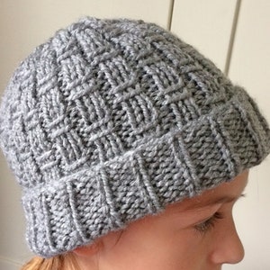 Peut inclure: Un bonnet en tricot gris avec un motif texturé. Le bonnet est porté sur la tête d'une personne.