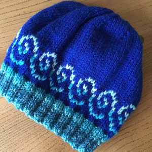 May include: A blue knitted hat with a white and blue patterned design. The hat has a blue and green brim.