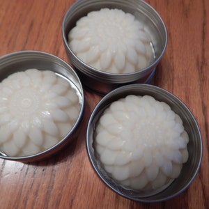 May include: Three small round metal tins with lids, each containing a white, flower-shaped solid. The solids have a raised, textured design.