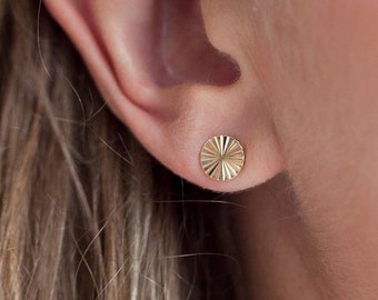 May include: A pair of gold stud earrings with a textured, circular design.