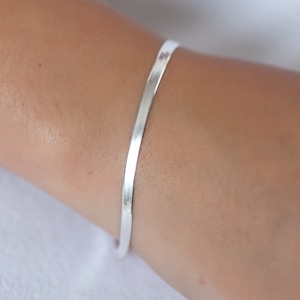 Op de afbeelding: Een zilveren kettingarmband om de pols van een persoon.