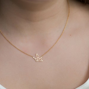 May include: A gold chain necklace with a delicate origami crane pendant.