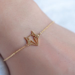 May include: A gold chain bracelet with a geometric fox pendant.
