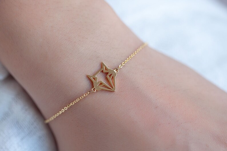 May include: A gold chain bracelet with a geometric fox pendant.
