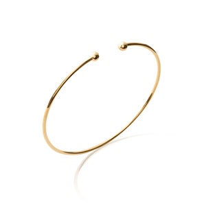May include: A simple gold bangle bracelet with rounded ends. The bracelet is made of a thin, smooth metal and has a polished finish.