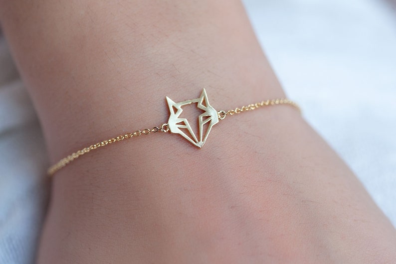 May include: A gold chain bracelet with a geometric fox pendant.
