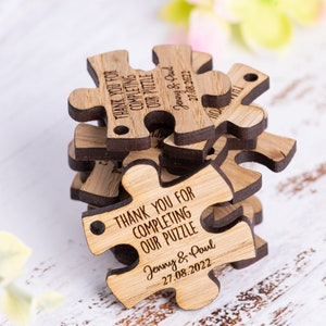 Puede incluir: Piezas de rompecabezas de madera con el texto "Gracias por completar nuestro rompecabezas" y los nombres "Jenny & Paul" y la fecha "27.08.2022".