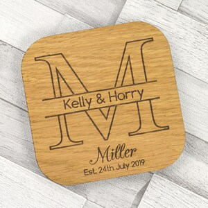 May include: Personalized wooden coaster with the letter "M" engraved in a large font. The text "Kelly & Harry Miller Est. 24th July 2019" is engraved below the letter.