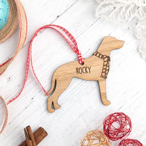 May include: Wooden dog ornament with a red and white ribbon, the dog is wearing a scarf and the ornament is personalised with the name "Rocky".