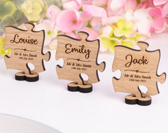 May include: Three wooden puzzle piece table place cards with the names Louise, Emily, and Jack. Each card has the text "Mr & Mrs Smith" and "14th July 2022" engraved on it.