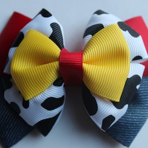 Puede incluir: Un lazo amarillo, rojo, blanco y azul con un estampado de vaca. El lazo está hecho de cinta y está atado en un nudo.