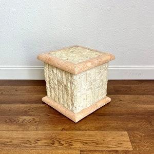 May include: A square, stone-textured side table with a light beige and peach color scheme. The table has a textured, stacked-stone appearance on the sides and a smooth top. The base and top edges are a peach color.