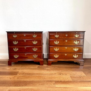 May include: A pair of matching wooden chests of drawers, each featuring four horizontal drawers with polished brass hardware. The wood has a rich, reddish-brown finish, and each drawer is equipped with two ornate brass pulls and a central keyhole.