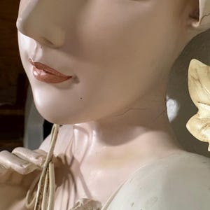May include: A white porcelain statue of a woman with a flowing white beige dress. The statue has a highly detailed face.