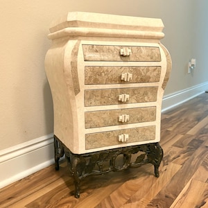 May include: A white and brown marbled chest of drawers with six drawers and ornate bronze legs. The chest is on a wood floor.