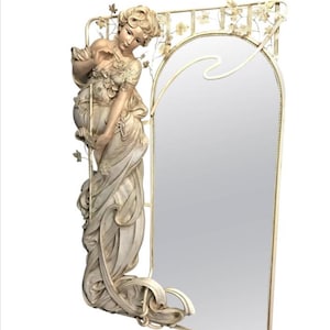 May include: A white, ornate mirror with a sculpted figure of a woman in a flowing gown. The mirror has a decorative frame with floral motifs and a curved top.