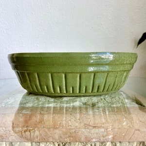 May include: A green ceramic bowl with a textured exterior. The bowl has a wide, shallow shape with vertical grooves around the sides. The bowl is sitting on a stone surface.