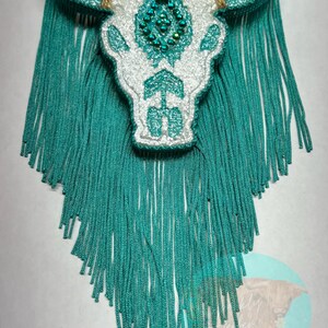 May include: White glitter bull skull with turquoise fringe. The skull has a beaded design on the forehead.
