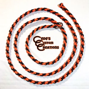 May include: Black and orange braided dog leash with a silver metal ring. The leash is coiled in a circle on a white background. The text "Cede's Custom Creations" is visible in the center of the image.