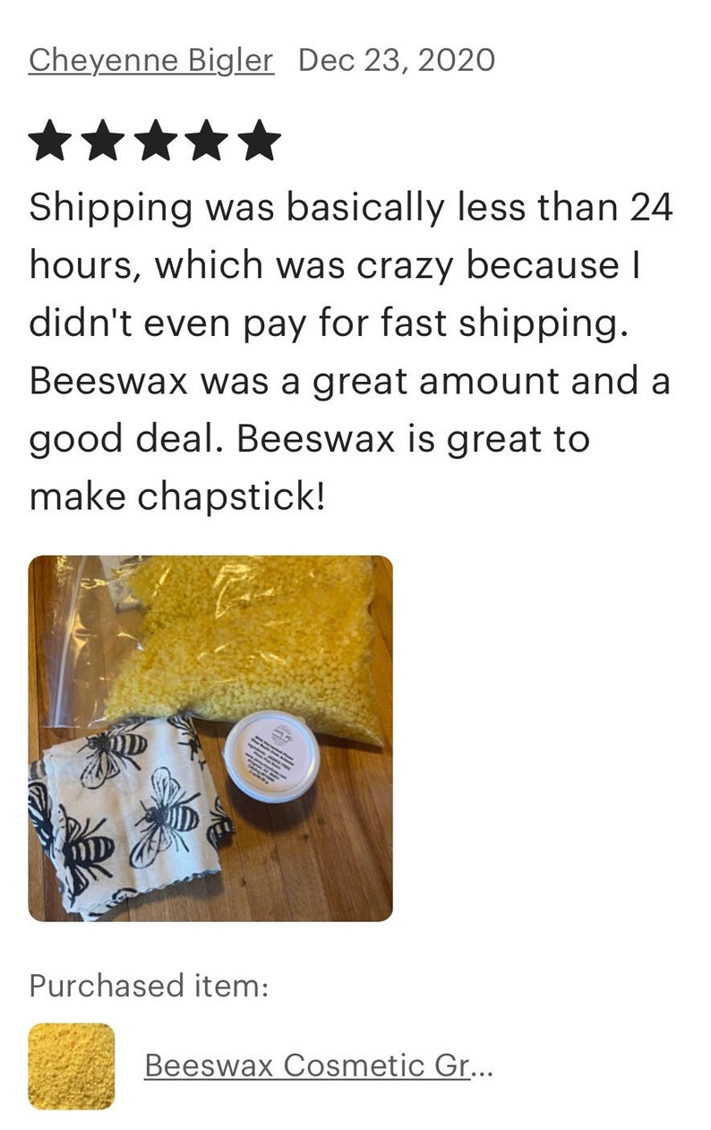 May include: A close-up of a bag of yellow beeswax pellets, a small white jar with a label, and a white fabric with a black bee pattern. The items are on a wooden surface. Beeswax Cosmetic Gr...