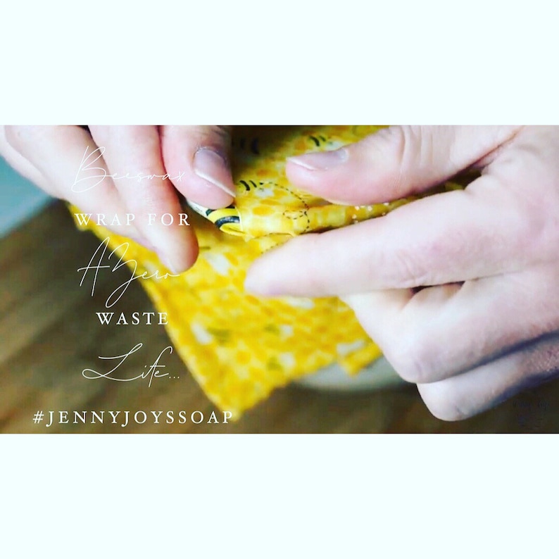 May include: A person's hands are shown wrapping a yellow and black beeswax food wrap. The wrap has a honeycomb pattern and the text "WRAP FOR A Zero WASTE Life... #JENNYJOYSSOAP" is printed on it.