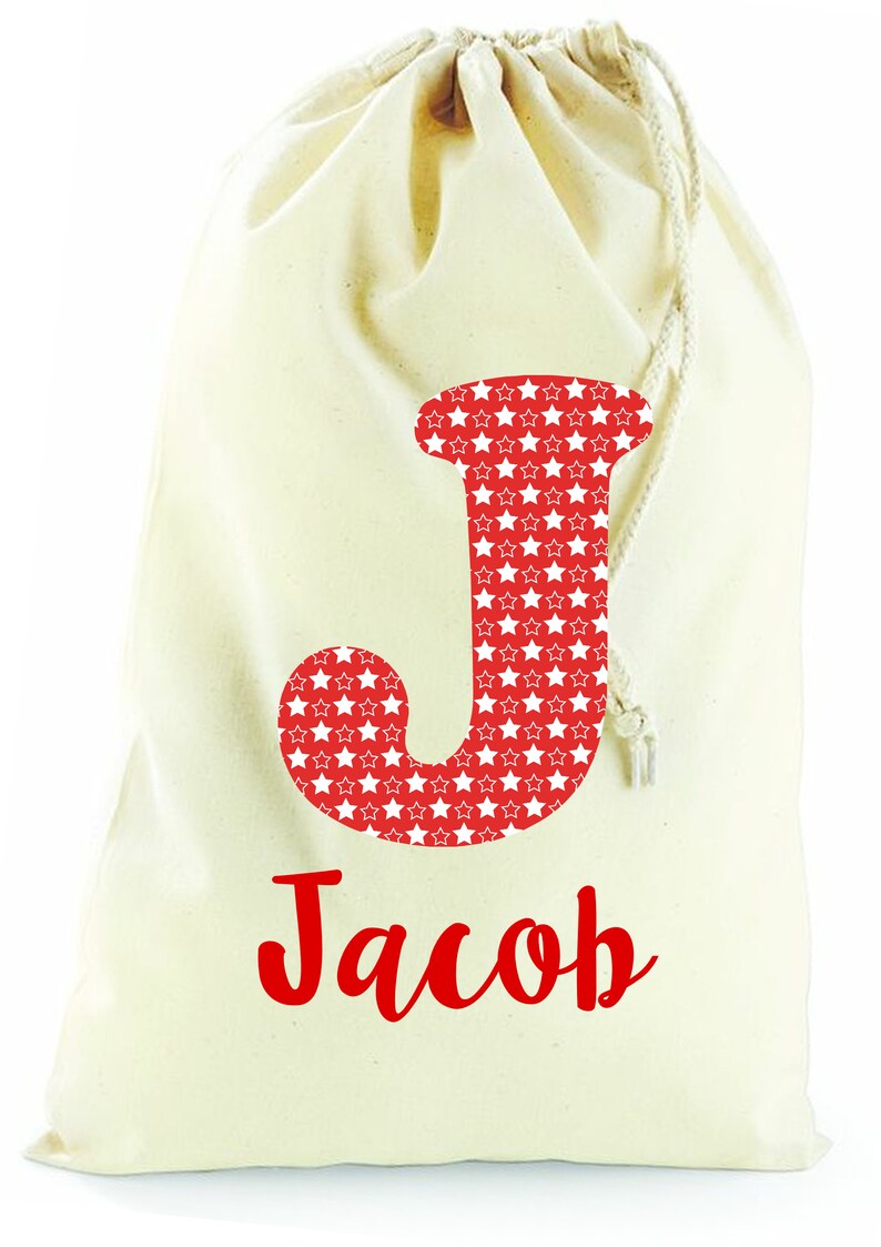May include: A white canvas drawstring bag with a red letter "J" with white stars on it. The name "Jacob" is written in red cursive below the letter.