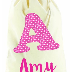 May include: A white canvas drawstring bag with a pink letter A covered in white stars and the name Amy written in pink below.