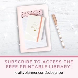 May include: A pink notebook with a white notepad and a smaller white notebook with the text "BUSY BUSY BUSY" and a bee icon. A gold pen with white stripes is on the right side of the image. The background is a white wooden surface with white stars.