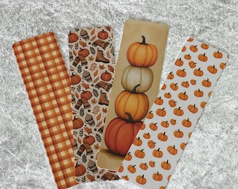 May include: Four fall-themed bookmarks. One has an orange and white plaid pattern. Another features pumpkins, boots, and scarves. The third shows stacked pumpkins, and the last has a pattern of small pumpkins.