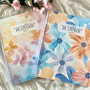 May include: Two spiral-bound "Everything Planner" notebooks with floral designs. One features orange and pink flowers, the other blue and orange. Each has the text "Everything Planner - 26/27-" on the cover.