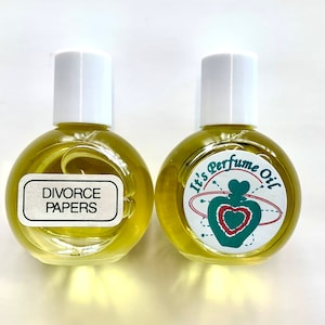 May include: Two small glass bottles with white caps. The bottle on the left has a label that says "Divorce Papers". The bottle on the right has a label that says "It's Perfume Oil" with a heart-shaped bottle design.