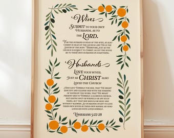 May include: A framed print with text from Ephesians 5:22-28, featuring the words "Wives" and "Husbands" in elegant script. The text is surrounded by olive branches and orange fruit on a cream background. The frame is a light wood colour.