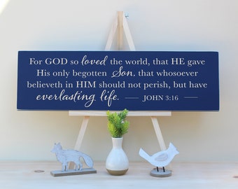 May include: A navy blue wooden sign with white text that reads "For GOD so loved the world, that HE gave His only begotten Son, that whosoever believeth in HIM should not perish, but have everlasting life. - JOHN 3:16". The sign is on a small wooden easel.