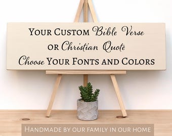 May include: A wooden sign on a small easel with the text "YOUR CUSTOM Bible Verse OR Christian Quote Choose YOUR FONTS AND COLORS." A small potted succulent sits below the sign. The bottom of the image reads "HANDMADE BY OUR FAMILY IN OUR HOME USING REAL WOOD AND REAL PAINT."