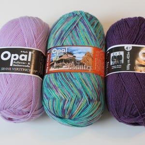 May include: Three skeins of Opal brand yarn in shades of lavender, teal with multicolored stripes, and deep purple. Each skein is labeled with the brand name and product details. The yarn is designed for sweaters and socks.