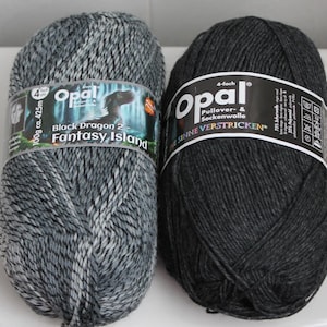 May include: Two skeins of Opal brand yarn. One is a mix of gray and white, labeled "Black Dragon 2 - Fantasy Island." The other is solid dark gray. Both have labels with the Opal logo and text. Each skein is 100g and approximately 425m.