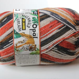 May include: A ball of Opal Regenwald Jubiläum yarn with a striped pattern in shades of orange, black, white, and tan. The label features a tiger illustration and text. The yarn is ca. 425m.