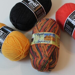 May include: Four skeins of Opal brand yarn in various colors. One skein is a variegated mix of orange, red, and blue with the word "Holidays" on the label. Other skeins are solid colors: black, red, and yellow. Each skein is labeled with the brand name and product details.