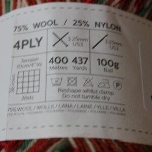 May include: Close-up of a ball of yarn with a label. The label indicates the yarn is 75% wool and 25% nylon, 4-ply, and 100g. It also shows needle sizes and washing instructions. The yarn has red, green, and white stripes.