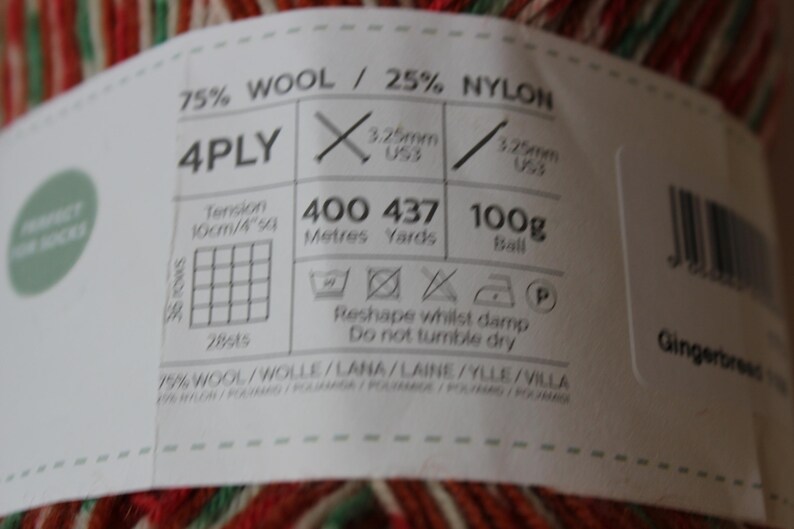 May include: Close-up of a ball of yarn with a label. The label indicates the yarn is 75% wool and 25% nylon, 4-ply, and 100g. It also shows needle sizes and washing instructions. The yarn has red, green, and white stripes.