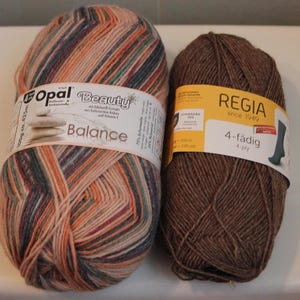 May include: Two skeins of yarn. One is multi-colored with orange, blue, and beige stripes, labeled "Opal Beauty Balance." The other is brown, labeled "Regia 4-fädig 4-ply."