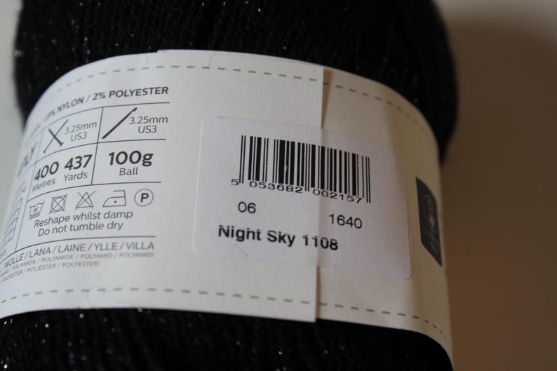 May include: A close-up of a black yarn ball with a label. The label indicates the yarn is Night Sky 1108, 100g, and 400 meters. It also specifies the needle size as 3.25mm, US3.