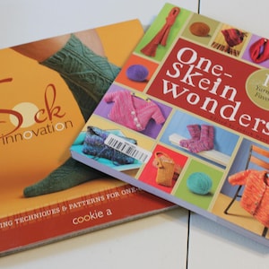 May include: Two knitting books, one titled "Sock Innovation" with a yellow cover and a sock on the front, and the other titled "One-Skein Wonders" with a red cover and a variety of colorful knitted items on the front.