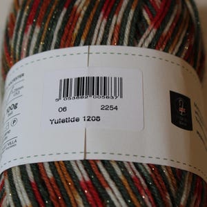 May include: A close-up of a yarn ball with a label. The yarn is a mix of red, green, gold, and white strands. The label has a barcode, the number "06", "2254", and "Yuletide 1208".