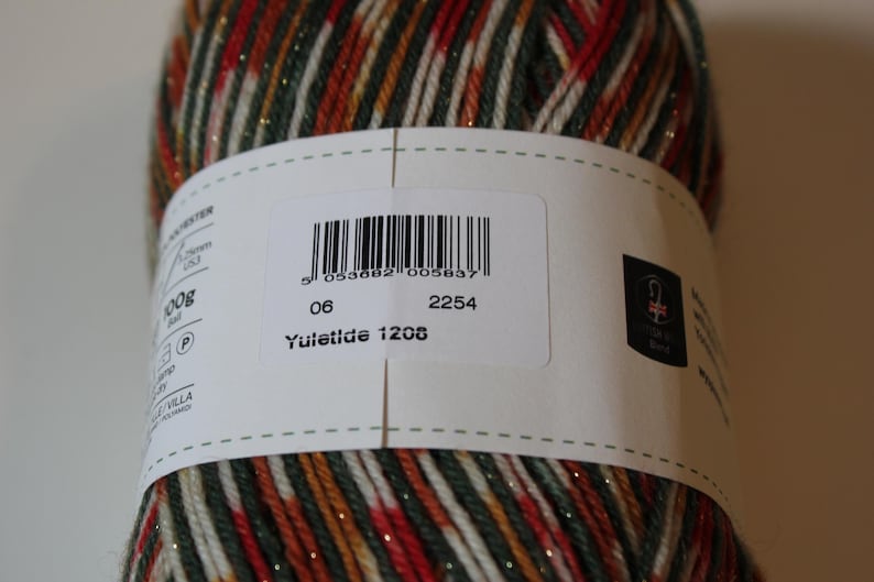 May include: A close-up of a yarn ball with a label. The yarn is a mix of red, green, gold, and white strands. The label has a barcode, the number "06", "2254", and "Yuletide 1208".