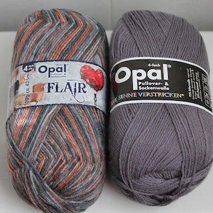 May include: Two skeins of Opal brand yarn. One is multi-colored with orange, gray, and black stripes, labeled "Flair." The other is solid gray. Both have labels with the brand name and "4-fach" on them. Each skein is 100g and approximately 425m.